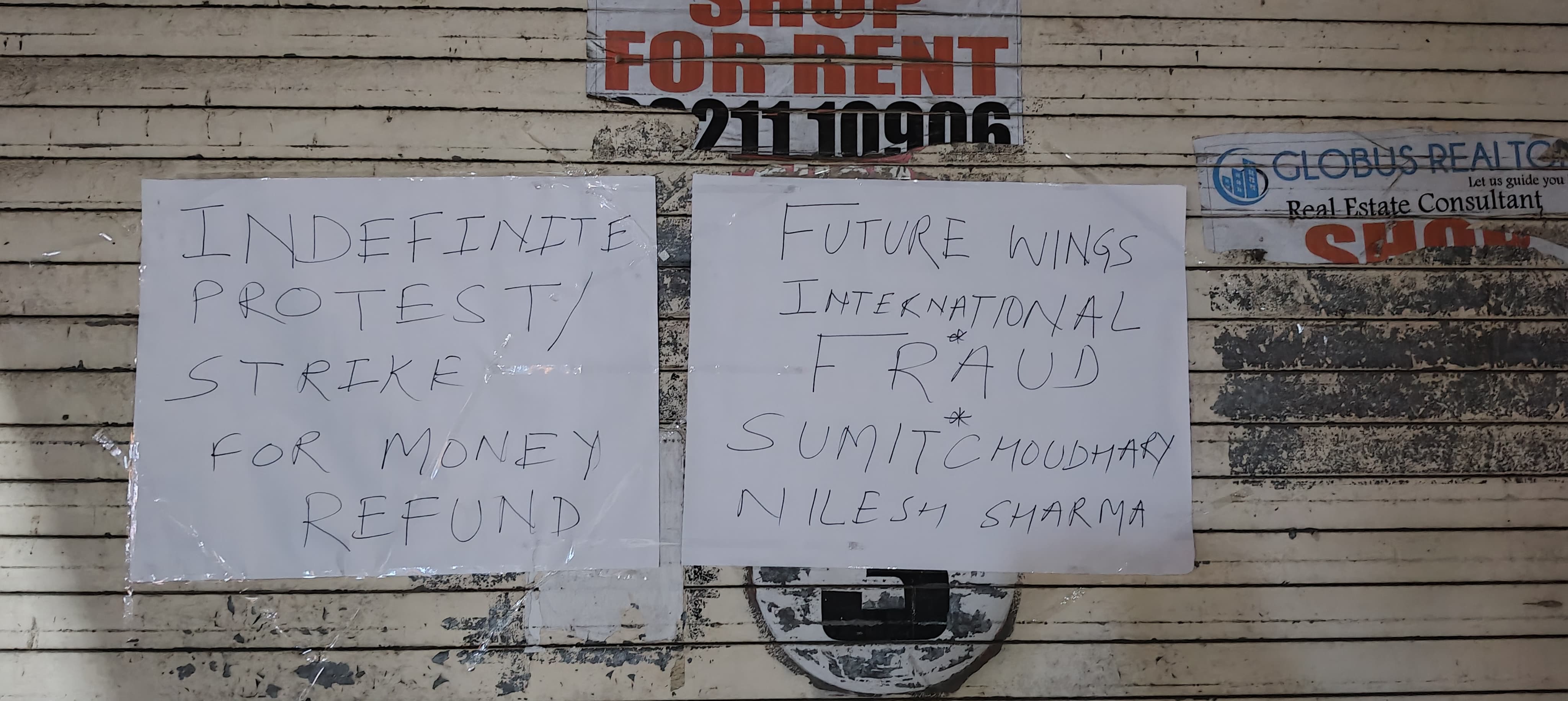 Handwritten protest signs on the office shutter naming Future Wings International and Sumit Choudhary